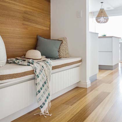 A built-in nook located at the front of the house with white padded seating, turquoise pillow and white straw hat